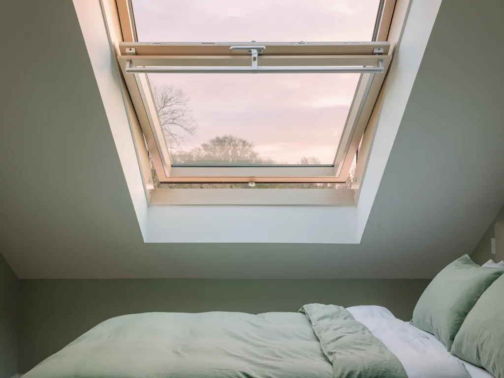 A still loft bedroom at dawn beneath a roof window